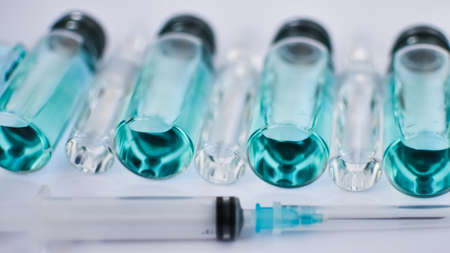 Vial vaccine, top view of glass ampoules with transparent and blue liquid, a syringe is lying near on white background, global vaccination conceptの写真素材