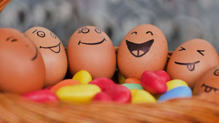 Stack of eggs with hand drawn faces on straw basket with colorful candy, easter preparation, holiday...
