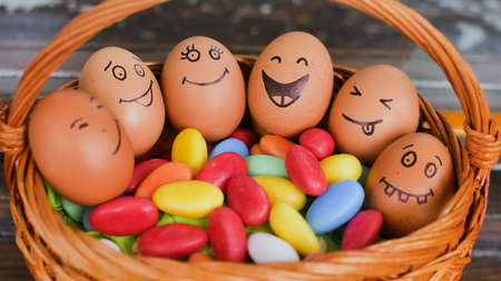 Stack of eggs with hand drawn faces on straw basket with colorful candy, easter preparation, holiday mood conceptsの写真素材