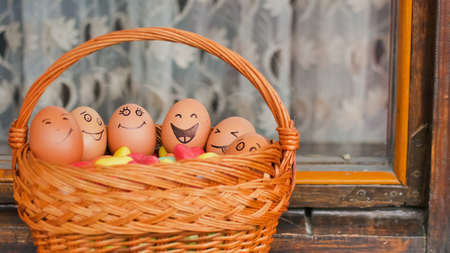 Stack of eggs with hand drawn faces on straw basket with colorful candy, easter preparation, holiday mood conceptsの写真素材