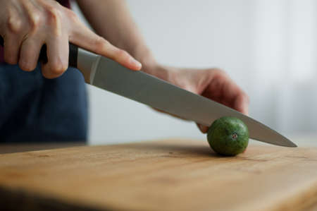 Female hands is cutting a fresh green feijoa fruit on a cut wooden board. Exotic fruits, healthy eating conceptの写真素材