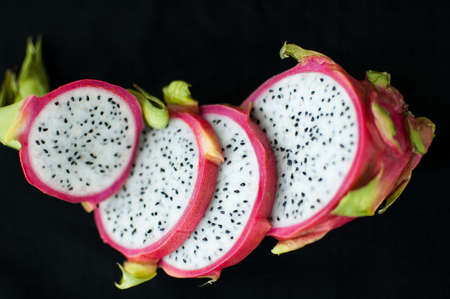 Slices of dragon fruit or pitaya with pink skin and white pulp with seeds on black background....