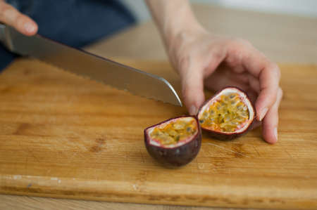 Female hands is cutting a fresh ripe passion fruit, maracuya on a cut wooden board. Exotic fruits, healthy eating conceptの写真素材