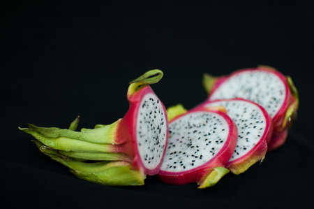 Slices of dragon fruit or pitaya with pink skin and white pulp with seeds on black background. Exotic fruits, healthy eating conceptの写真素材