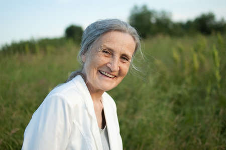 Portrait of senior woman with grey hair and face with wrinkles wearing white jacket and relaxing at...