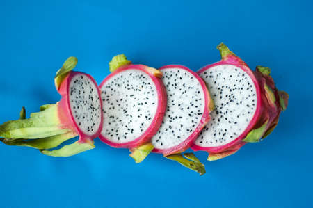 Slices of dragon fruit or pitaya with pink skin and white pulp with black seeds on blue background. Exotic fruits, healthy eating conceptの写真素材