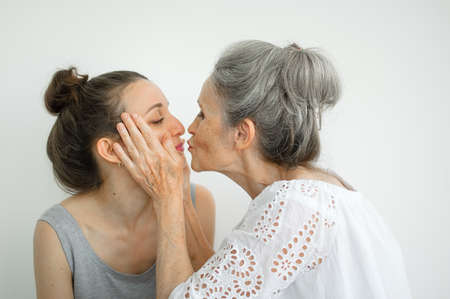 Happy senior mother is hugging her adult daughter, the women are laughing together, sincere family of different age generations having fun on white backgroundの写真素材