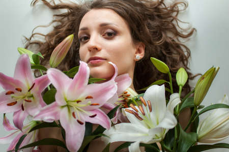 Top view of beautiful woman lying on the table with perfect bouquet of beautiful lilies, female portrait conceptの写真素材