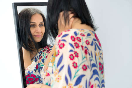 Studio photo of middle aged woman starting getting grey-haired wearing dress with flowers on white...