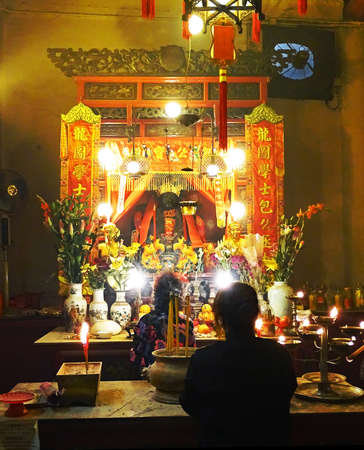 Sheung Wan, Hong Kong - February 10, 2016: Two women pray at on altar inside the Man Mo Temple in Sheung Wan, Hong Kong. On the altar are incense sticks, candles, flowers and oranges. The temple which built in 1847 and is dedicated to the gods Man Cheong のeditorial素材