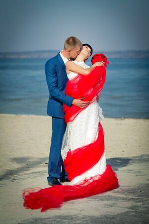 the groom and the bride on a beach with red tulleの写真素材