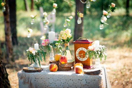 Wedding decor for photographing with the bracket clock, flowers, candles and peaches on a ancient suitcase. Roses in bulbs on a background . Decoration of a wedding photoshoot.  Details of a wedding decor.の写真素材