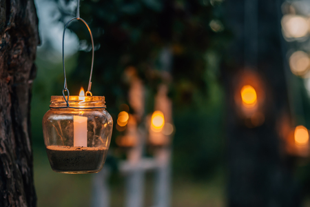 The lamp made of a jar with a candle  is  hanging  on a tree at night. Wedding night decor. Night ceremony