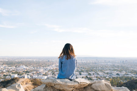 Young woman sitting on top of a mountain looking at the city.の写真素材