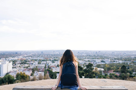 Back view of a young woman sitting on the top of a mountain and looking at the cityの写真素材