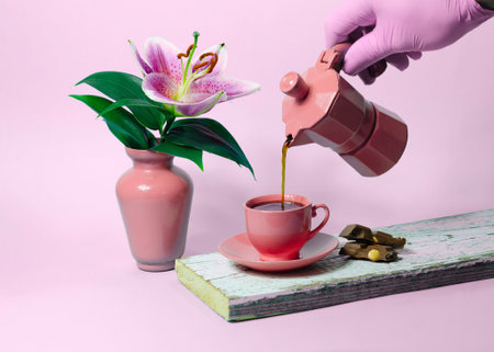 Female hand in a pink glove pours tea from a teapot into a pink cup.の写真素材