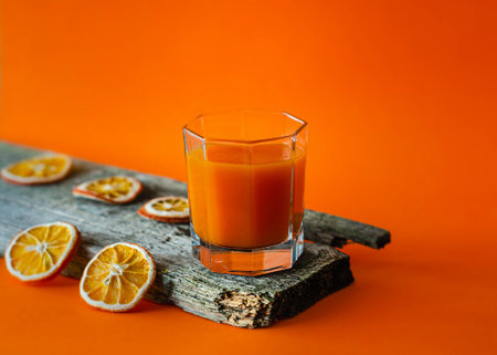 Glass of fresh orange juice on a wooden log. Orange background.の写真素材