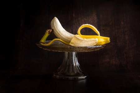 Peeled banana in a glass bowl on a dark wooden background.の写真素材
