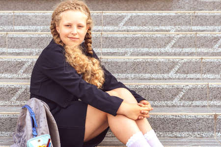Schoolgirl with a backpack sitting on the steps in front of the school. Concept school days, Back to...