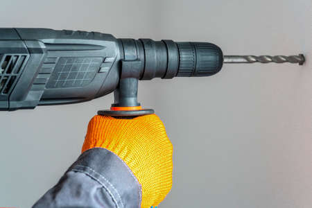 workman hand with a rotary hammer. Hands in protective gloves with hammer drill perforator. close upの写真素材
