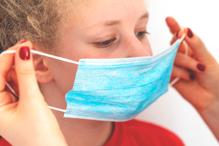 Child in protective mask. Mom puts her daughter a mask on her face. Infectious disease protection...