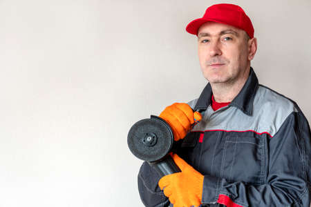 The worker is holding a grinding machine with a disk. Man in uniform with a tool.の写真素材
