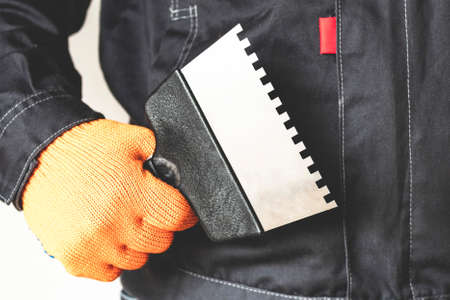Spatula in the hand of a worker. Working tools. gloves, bubble level, trowel. Worker gear conceptの写真素材
