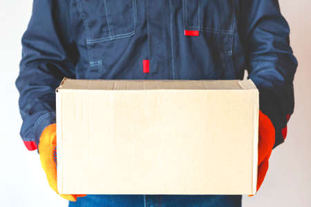 delivery man holding package. Courier holding box. man carrying cardboard with copy space. close upの写真素材