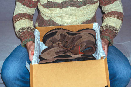 The man holds a box with shoes in hands. Concept of buying, trying on shoes and boots.close-up.の写真素材