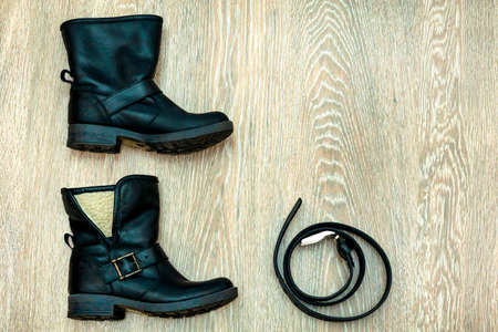 Two black leather women's boots and belt on a gray background. Women's shoes and accessory