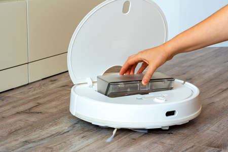 White robot vacuum cleaner.Garbage container. close up. Woman's hand holding a container with...
