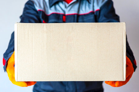 delivery man holding package. Courier holding box. man carrying cardboard with copy space. close upの写真素材