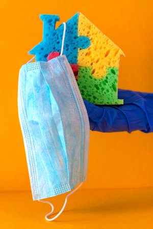Hand in glove holds house and face mask.The concept of disinfection and sanitary protection of...