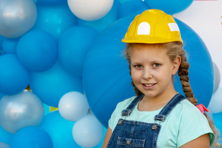Cheerful kid in a builder's protective helmet. A happy child in clothing builder. Portrait of a beautiful girl with a smileの写真素材