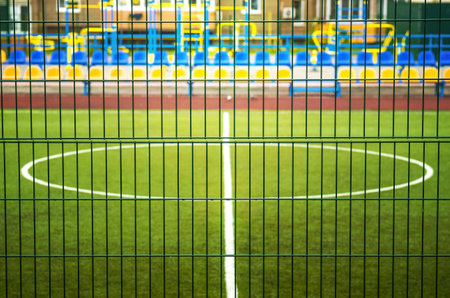 Football field with artificial lawn. ground training near the apartment building.Central circle of stadium. The football field is fenced with a green iron lattice.の写真素材