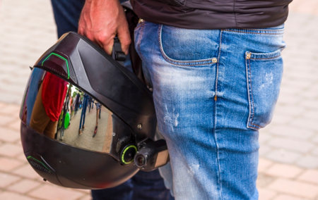 The man holds a motorcycle helmet in hand. Closeup picture of a Brutal biker man keep black...