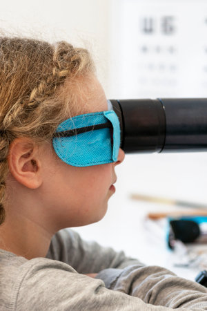 A girl is sitting in front of a device for stimulating vision.Ophthalmic equipment. Orthoptic and Pleoptic Therapy. Concept of recovery and training of vision. The concept of vision treatment children.の写真素材