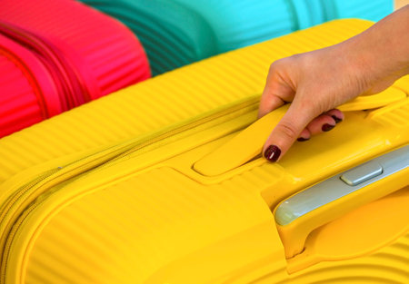 hand holds a suitcase for the handle. Bags for a trip. Colored Bags. Concept moving, travel, trip, flight. Concept Summer rest, holidays. Choosing a suitcase for travel.の写真素材