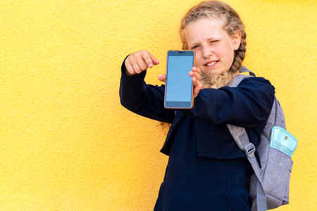 girl holds a smartphone. Concept use of gadgets by children, online training, online learning, online education. problem using tablets and gadgets. girl in a uniform. copy spaceの写真素材