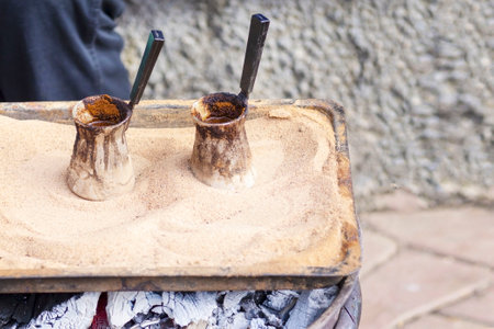 Traditional Turkish coffee prepared on hot sand.. Two cezves filled with hot oriental coffee. Two...