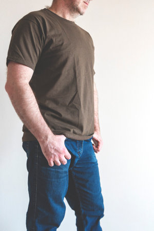 Man dresses, tries on a T-shirt. man wearing t-shirt and jeans, standing. Concept fitting trying on clothes. Copy spaceの写真素材