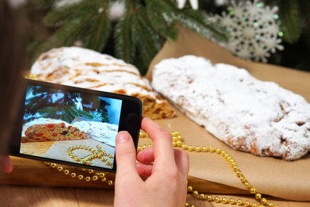 Hands are holding a smartphone. Photographing christmas cake, Stollen, homemade pie, Home baking conceptの写真素材