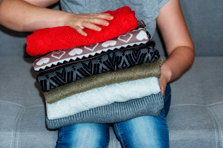 A stack of sweaters, jumpers in female hands. Girl holds hands bunch of knitted warm winter clothes. Fall winter season fashionable knitwear.の写真素材