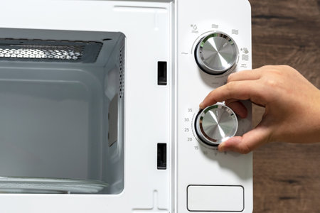 hand using an oven. Girl Adjusting Temperature Of Microwave Oven.Using microwave oven. power regulator, temperature controlの写真素材