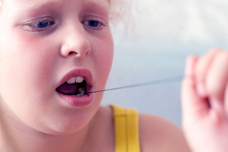 girl holds thread to pull out a milk tooth. Removal of tooth at the child. The concept loss of milk...