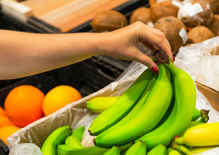 The female hand takes fresh fruit in a supermarket close-up. woman choosing fresh bananas in store. The concept of buying fruit. Shopper conceptの写真素材