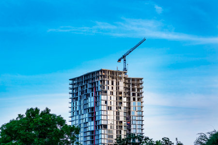 The construction crane and the building against the blue sky. Construction of a high-rise building...
