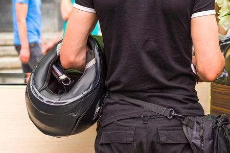 The man holds a motorcycle helmet in hand. Closeup picture of a Brutal biker man keep black...