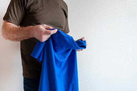 Man dresses, tries on a T-shirt. man wearing t-shirt, standing. Concept fitting trying on clothesの写真素材