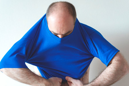 Man dresses, tries on a T-shirt. man wearing t-shirt and jeans, standing. Concept fitting trying on clothesの写真素材